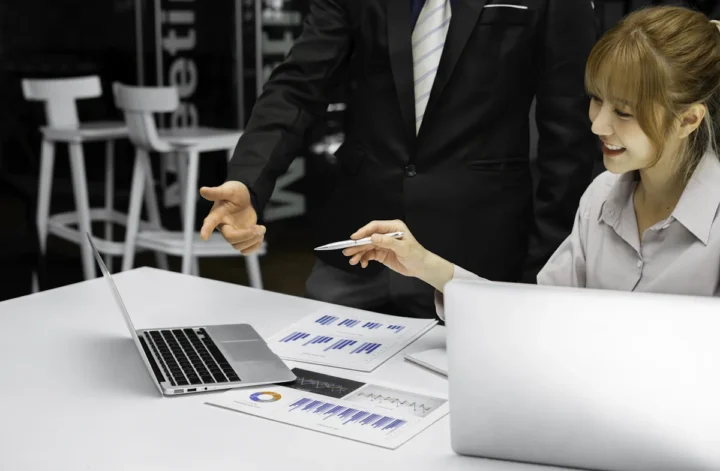 Une femme qui discute avec un homme en regardant un écran d'ordinateur posé sur le bureau
